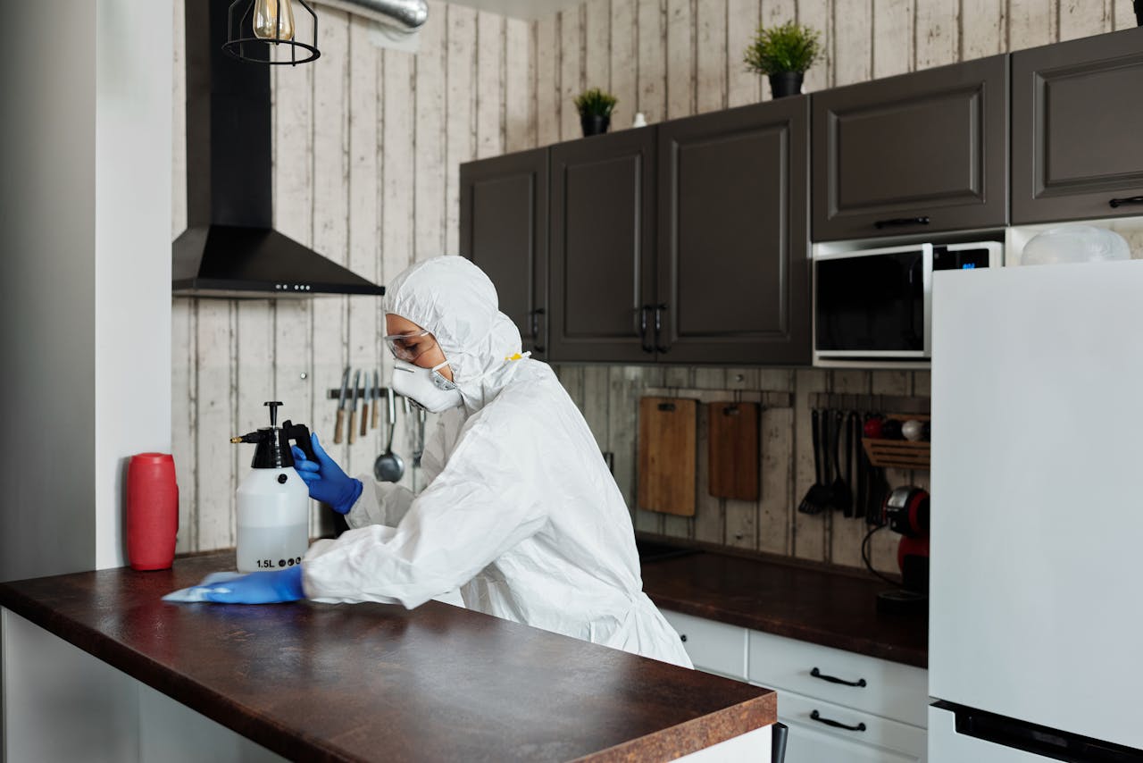 services-03 A worker in protective gear disinfects a kitchen, ensuring a clean and safe environment.