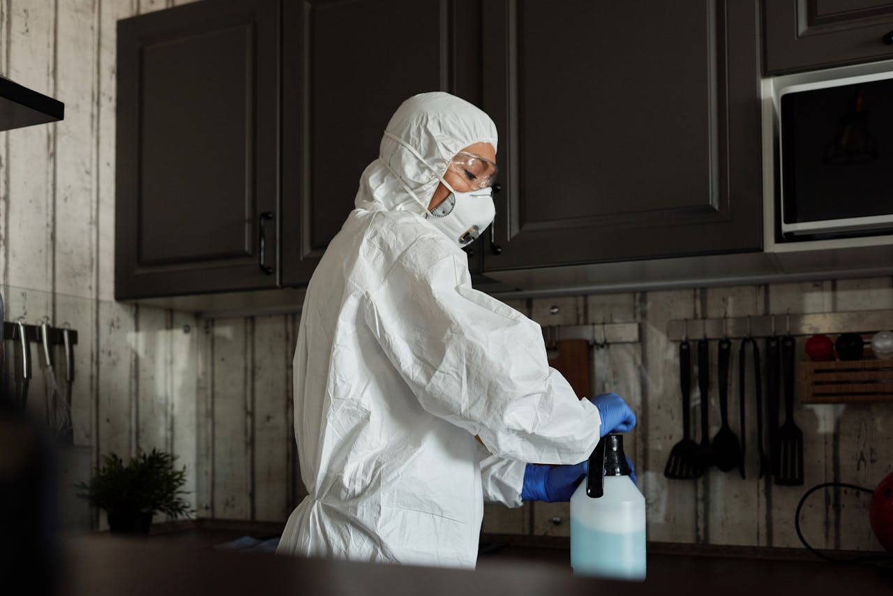 about-01 Healthcare worker in PPE uses disinfectant spray in a kitchen setting during COVID-19 pandemic.