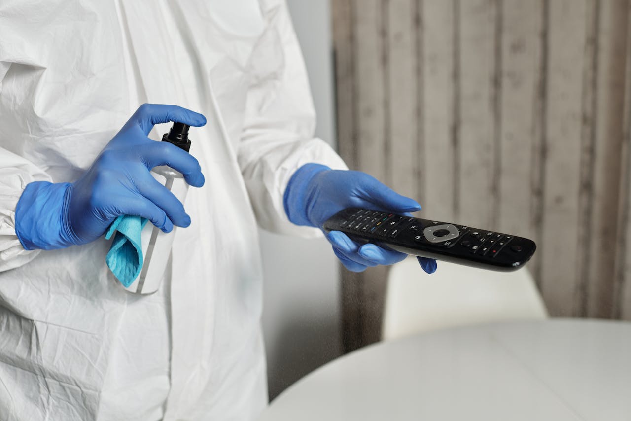 services-01 Hands in gloves disinfecting a remote control indoors. Pandemic hygiene concept.